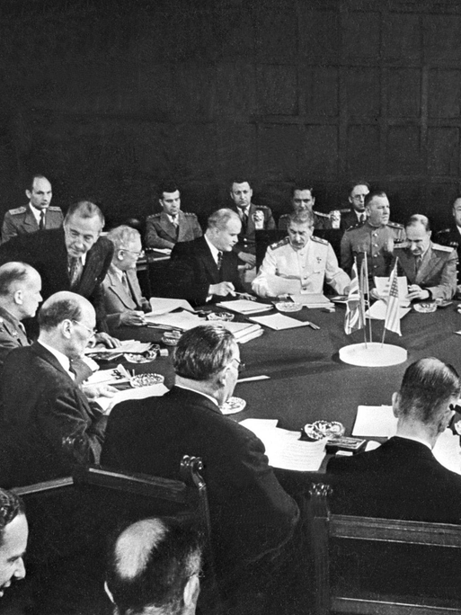 Historisches Schwarzweißfoto von Männer, die bei der Potsdamer Konferenz um einen runden Tisch herum sitzen.