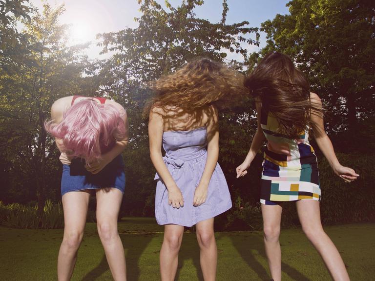 Drei tanzende junge Frauen in einem sommerlichen Park.