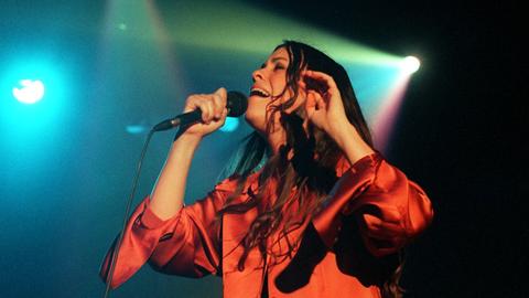 Die kanadische Sängerin und Songschreiberin Alanis Morissette mit offenem langen Haar singend auf einer Bühne mit grellem Scheinwerferlicht.