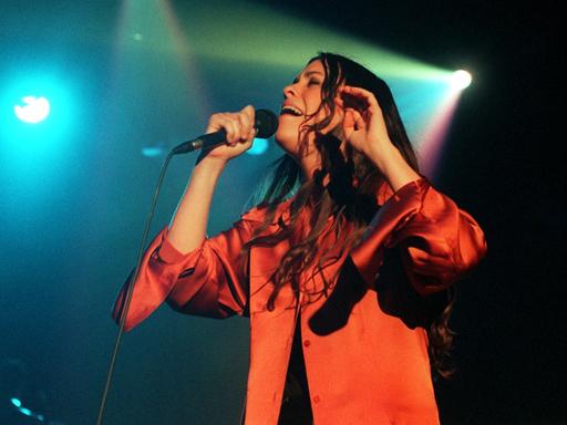Die kanadische Sängerin und Songschreiberin Alanis Morissette mit offenem langen Haar singend auf einer Bühne mit grellem Scheinwerferlicht.