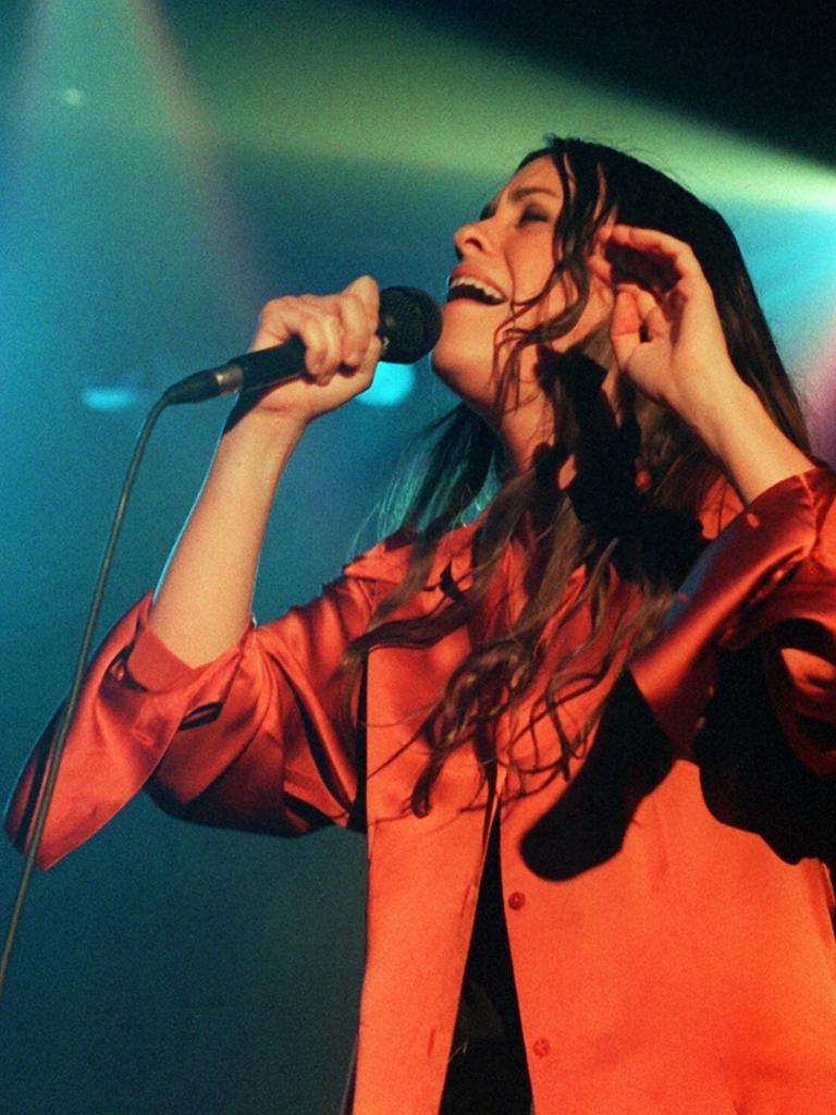 Die kanadische Sängerin und Songschreiberin Alanis Morissette mit offenem langen Haar singend auf einer Bühne mit grellem Scheinwerferlicht.