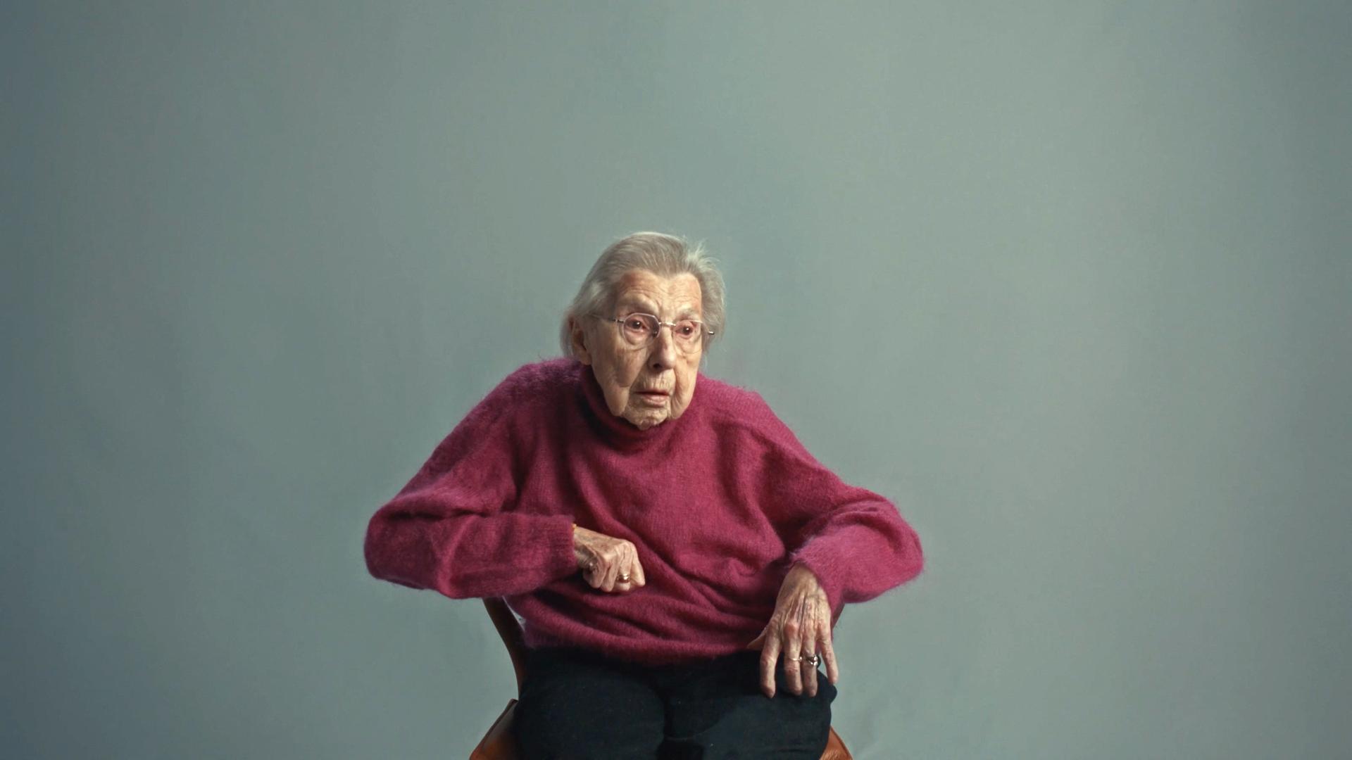 Eine alte Frau mit Brille sitzt auf einem Stuhl und schaut in die Kamera. Es ist ein Ausschnitt aus einem Werbe-Film von dem Europäischen Parlament.