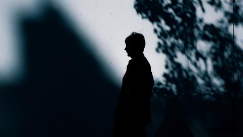 Eine Frau in einemf Parkt steht seitlich vor einem Schatten.