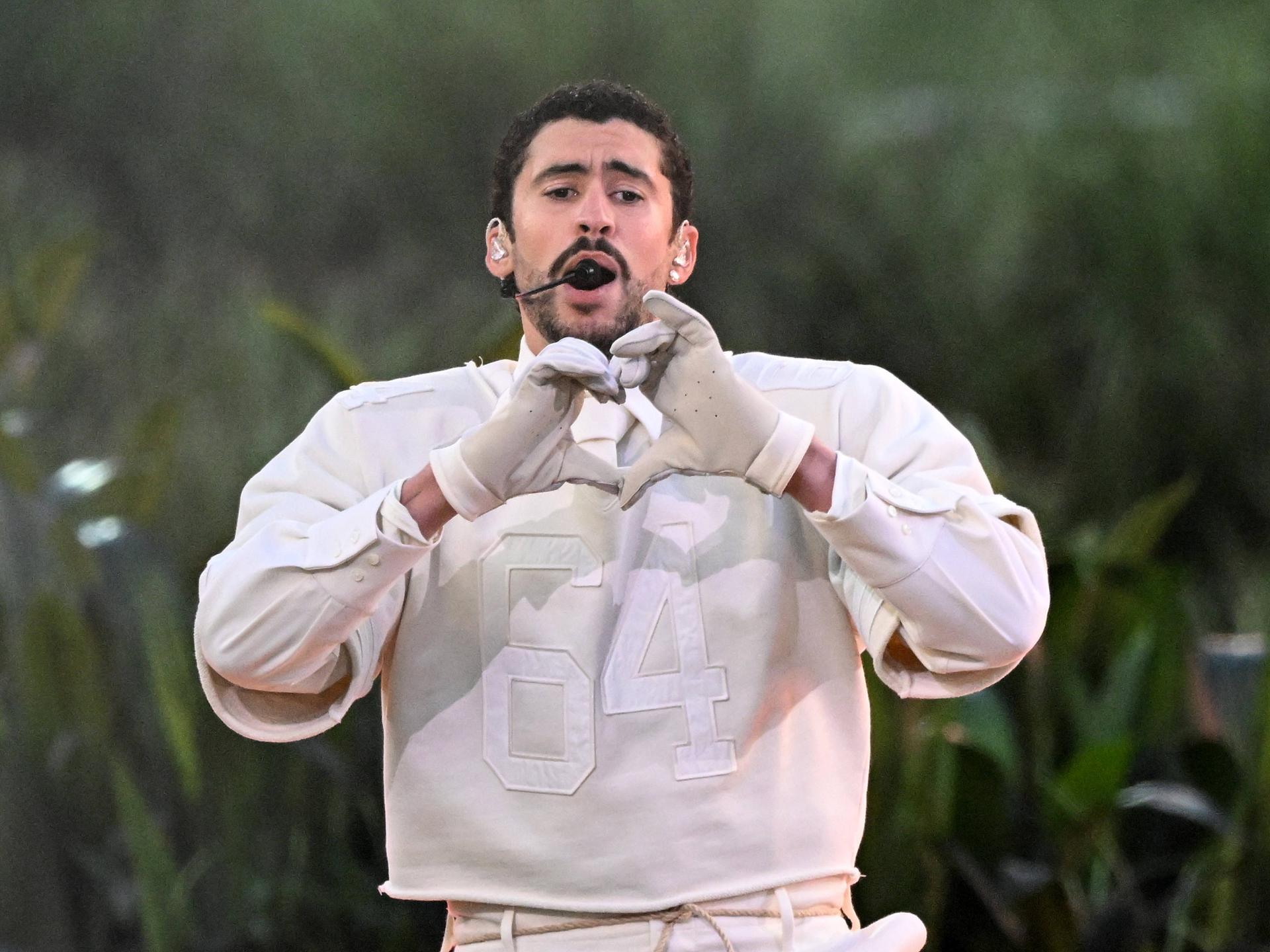 Der Musiker Bad Bunny formt singend auf der Bühne mit seinen Händen ein Herz.