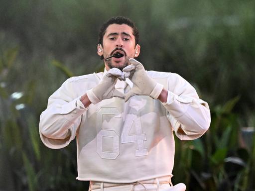 Der Musiker Bad Bunny formt singend auf der Bühne mit seinen Händen ein Herz.