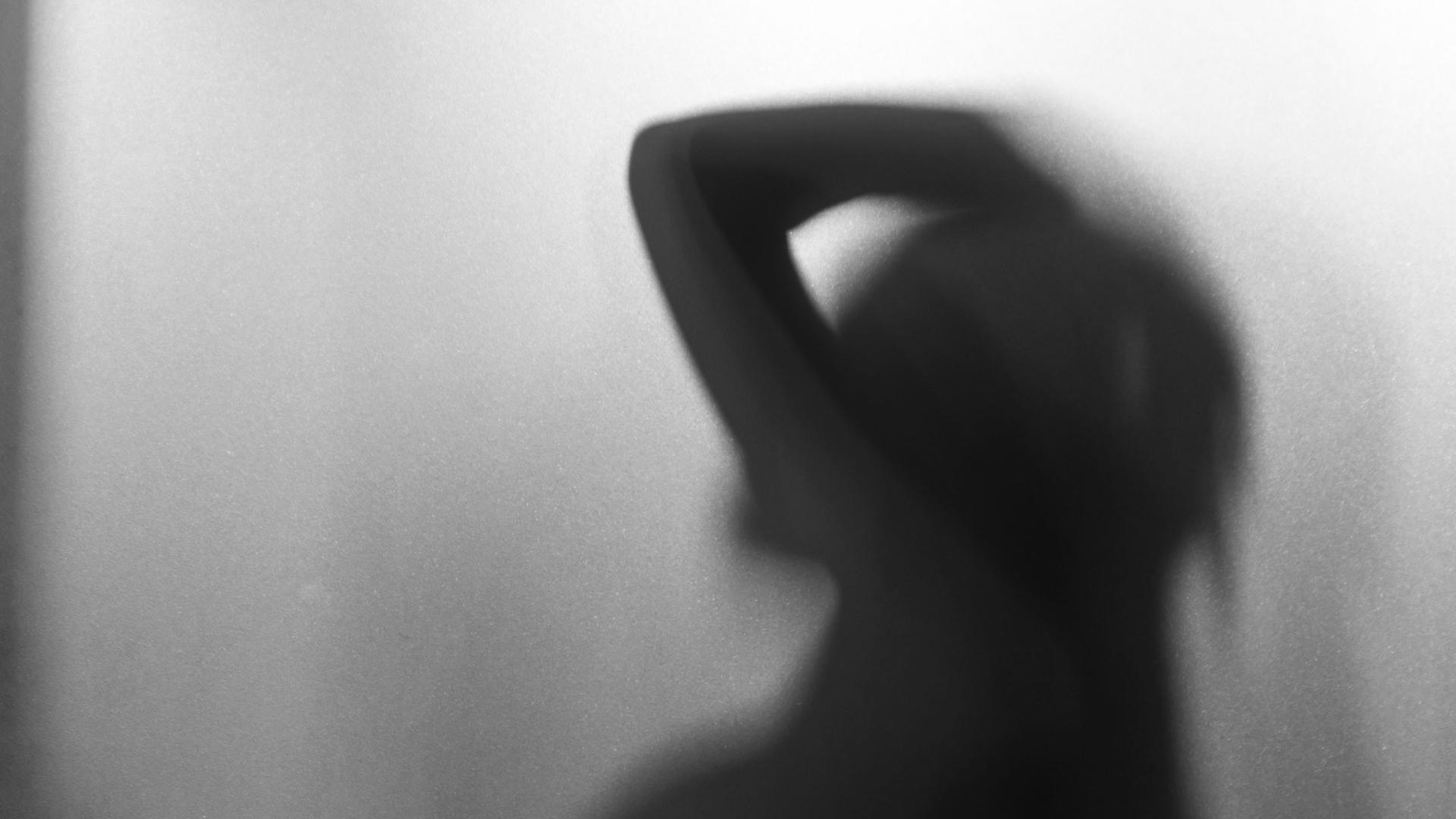 Die Silhouette einer weiblichen Person hinter eine Milchglasscheibe.