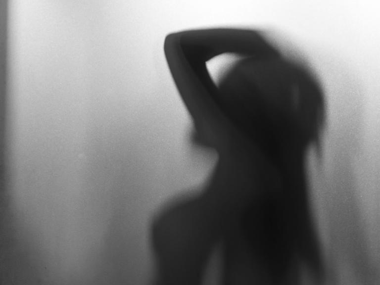 Die Silhouette einer weiblichen Person hinter eine Milchglasscheibe.