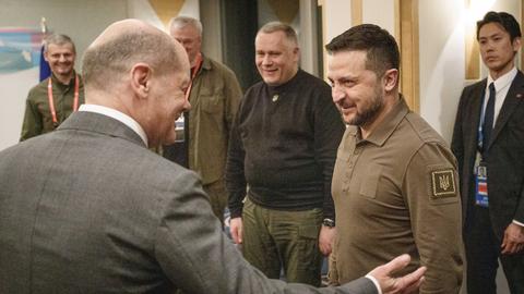 Bundeskanzler Olaf Scholz begrüsst den ukrainischen Präsidenten Wolodymyr Selenskyi. Beide lächeln. Scholz macht eine einladende Geste. Im Hintergrund stehen mehrere Personen und schauen zu.