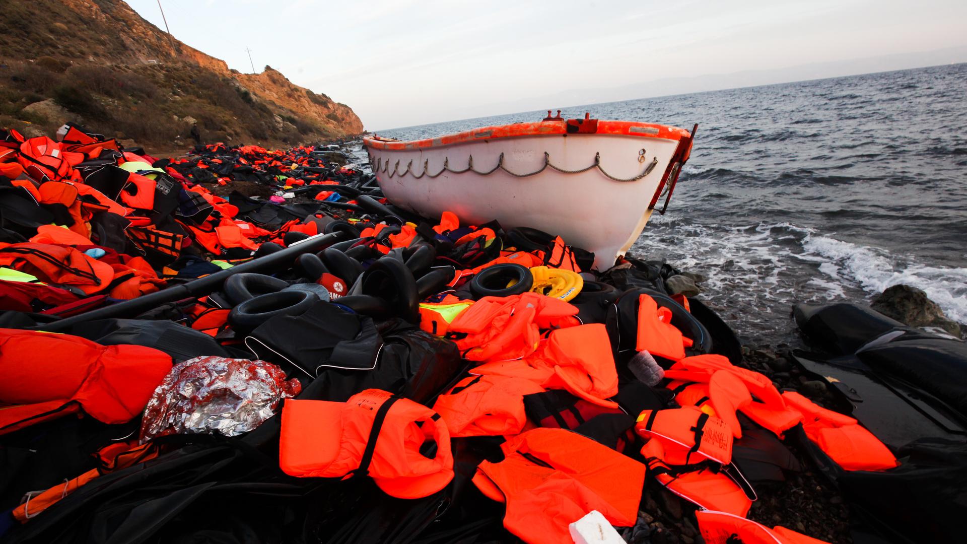 Ein Boot und ein Berg Rettungswesten liegen an der Küste von Lesbos. (2015) Ein Boot und ein Berg Rettungswesten liegen an der Küste von Lesbos. (2015)