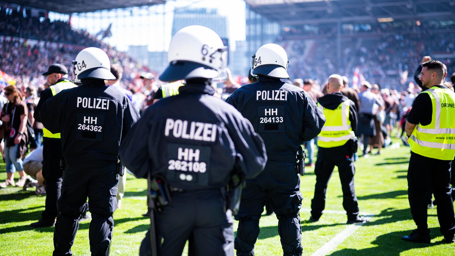 Polizisten stehen im Feld eines Fußballstadions bei einer Partie zwischen dem FC St. Pauli und dem VfL Osnabrück, im Hintergrund sind Fans auf den Rängen zu sehen.