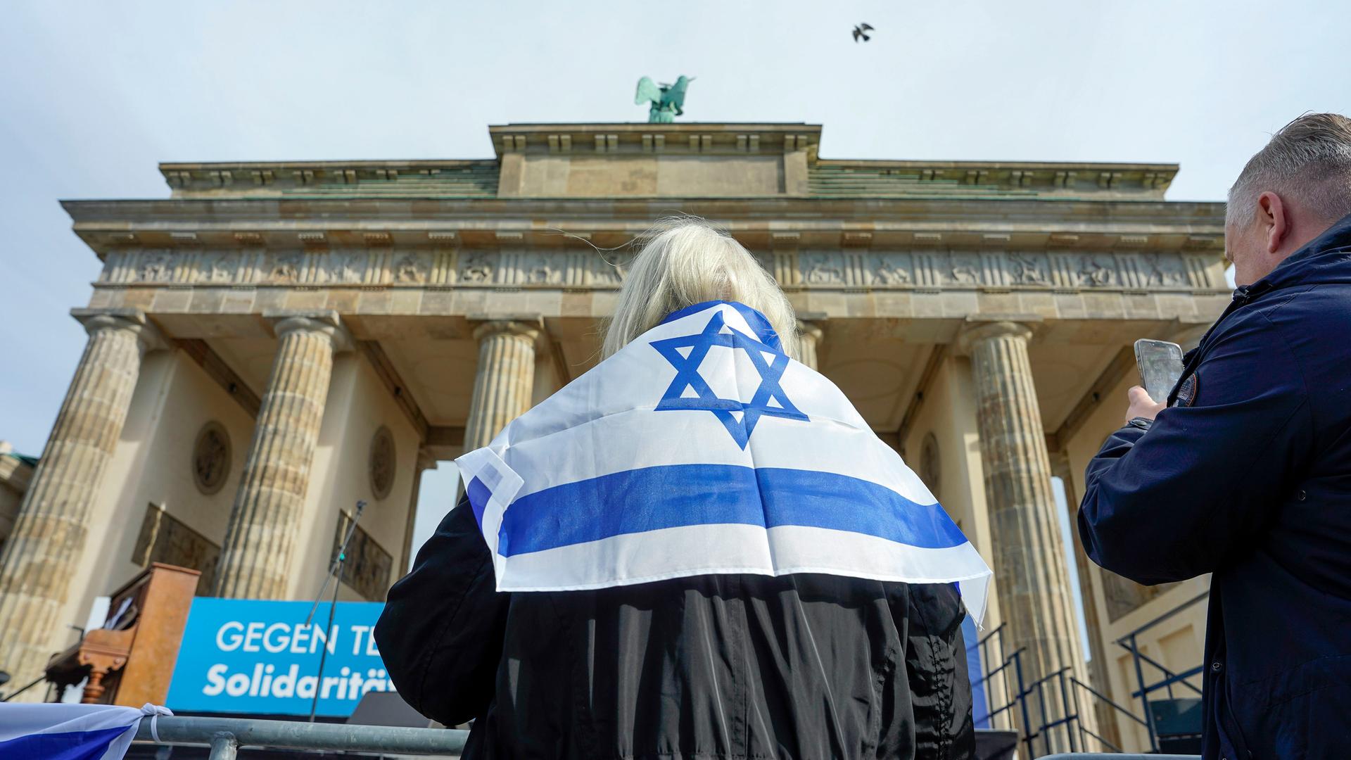 Eine Frau steht mit einer Israelflagge um die Schultern vor dem Brandenburger Tor in Berlin.