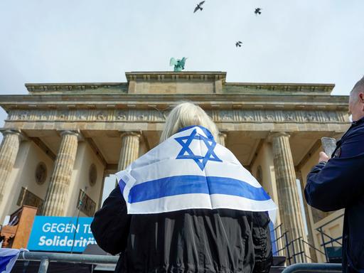 Eine Frau steht mit einer Israelflagge um die Schultern vor dem Brandenburger Tor in Berlin.