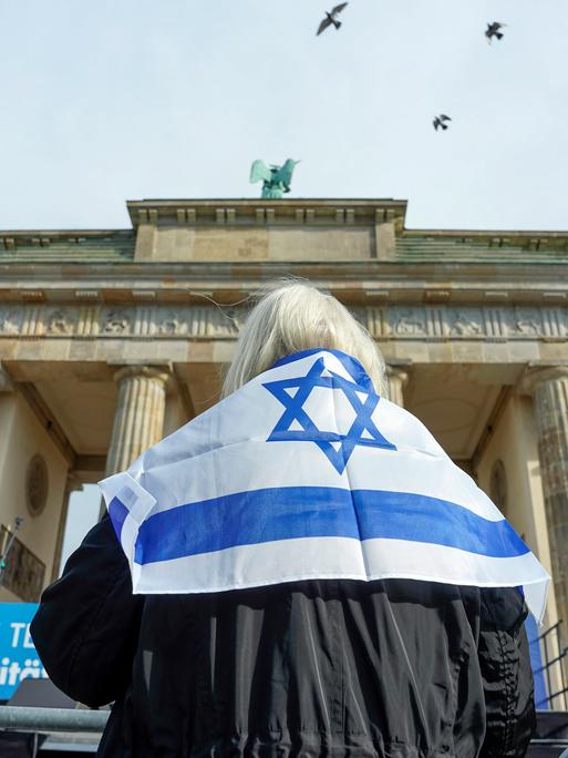 Eine Frau steht mit einer Israelflagge um die Schultern vor dem Brandenburger Tor in Berlin.