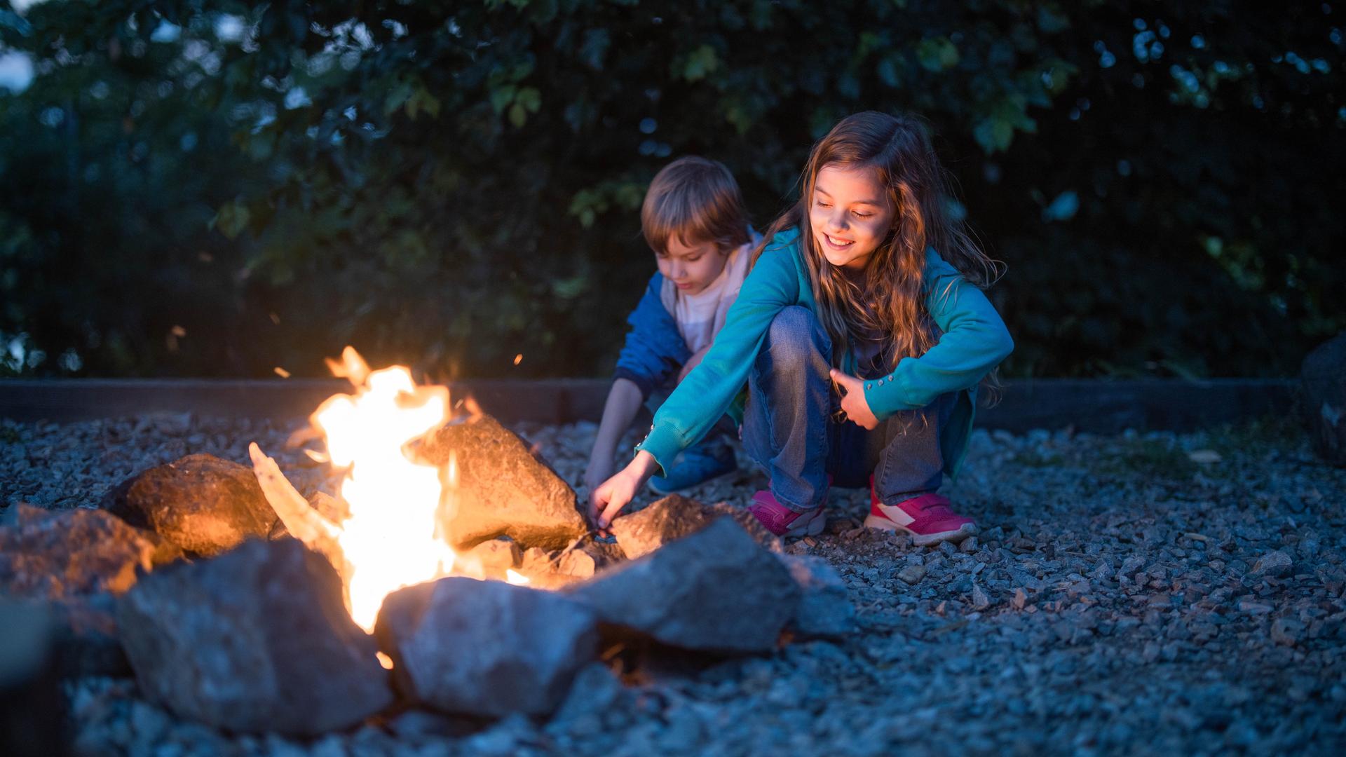 Zwei Kinder hocken an einem kleinen Feuer.