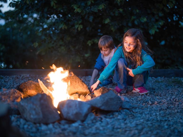 Zwei Kinder hocken an einem kleinen Feuer.