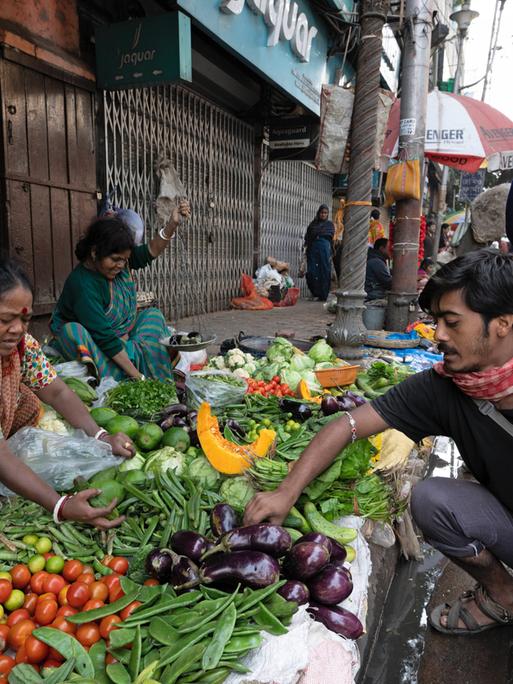 Auf einem Markt im indischen Kolkata reicht eine Händlerin einem Kunden Gemüse.