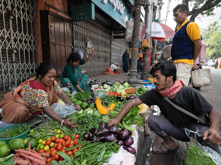 Auf einem Markt im indischen Kolkata reicht eine Händlerin einem Kunden Gemüse.