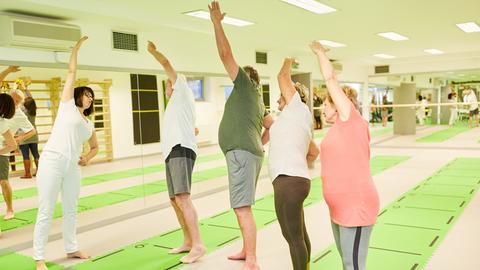 Trainer oder Physiotherapeutin zeigt Senioren eine Stretching-Übung bei der Rückengymnastik.