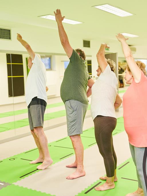 Trainer oder Physiotherapeutin zeigt Senioren eine Stretching-Übung bei der Rückengymnastik.