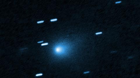 Der interstellare Komet 3I/ATLAS aufgenommen mit dem Hubble Space Teleskop am 21. Juli 2025. Die Aufnahme zeigt vor schwarzem Hintergrund helle Lichtflecken. Ungefähr in der Mitte ist ein größerer Lichtfleck mit Aura.