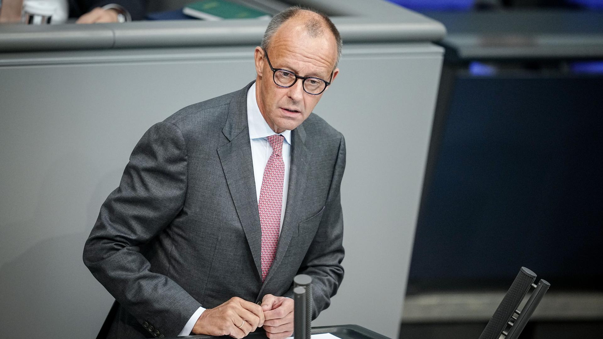 Friedrich Merz steht am Redepult des Bundestags und spricht mit ernster Mine zu den Abgeordneten.