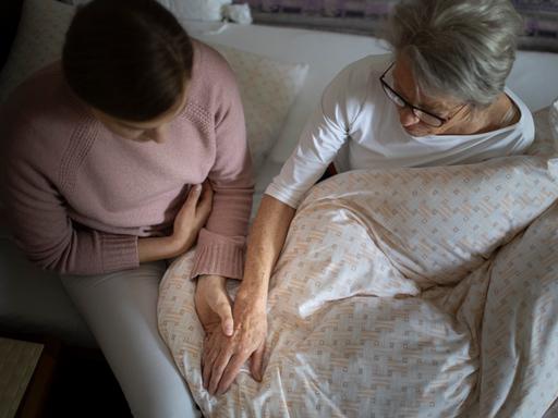 Eine jüngere Frau hält die Hand einer älteren Frau.