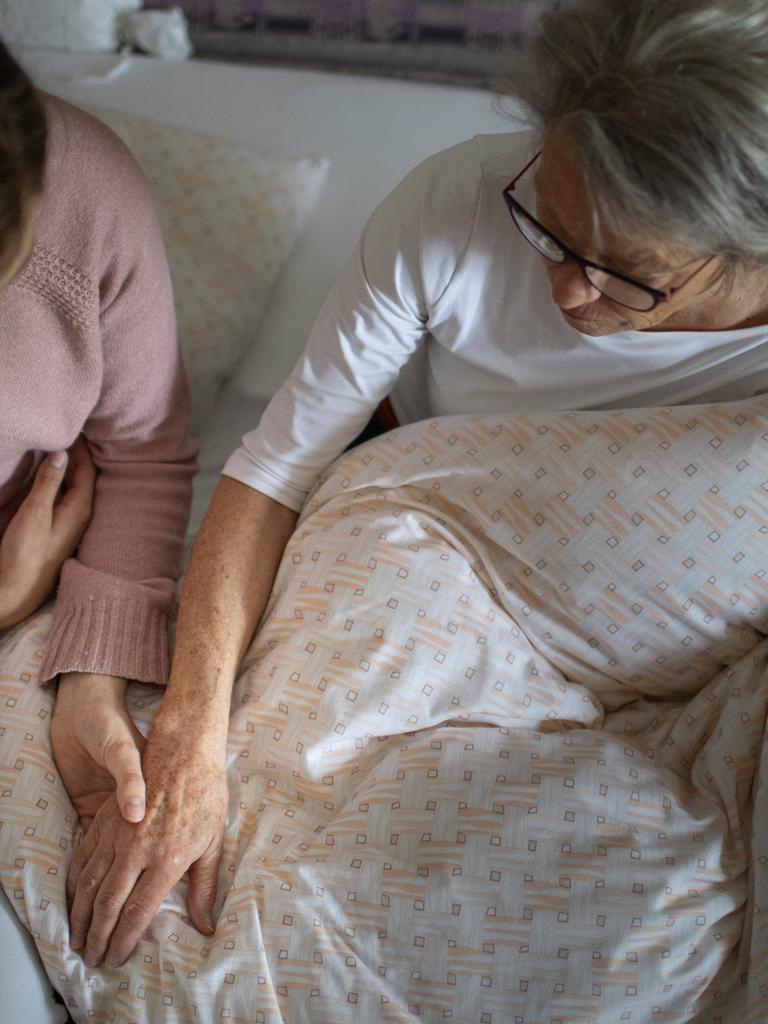 Eine jüngere Frau hält die Hand einer älteren Frau.