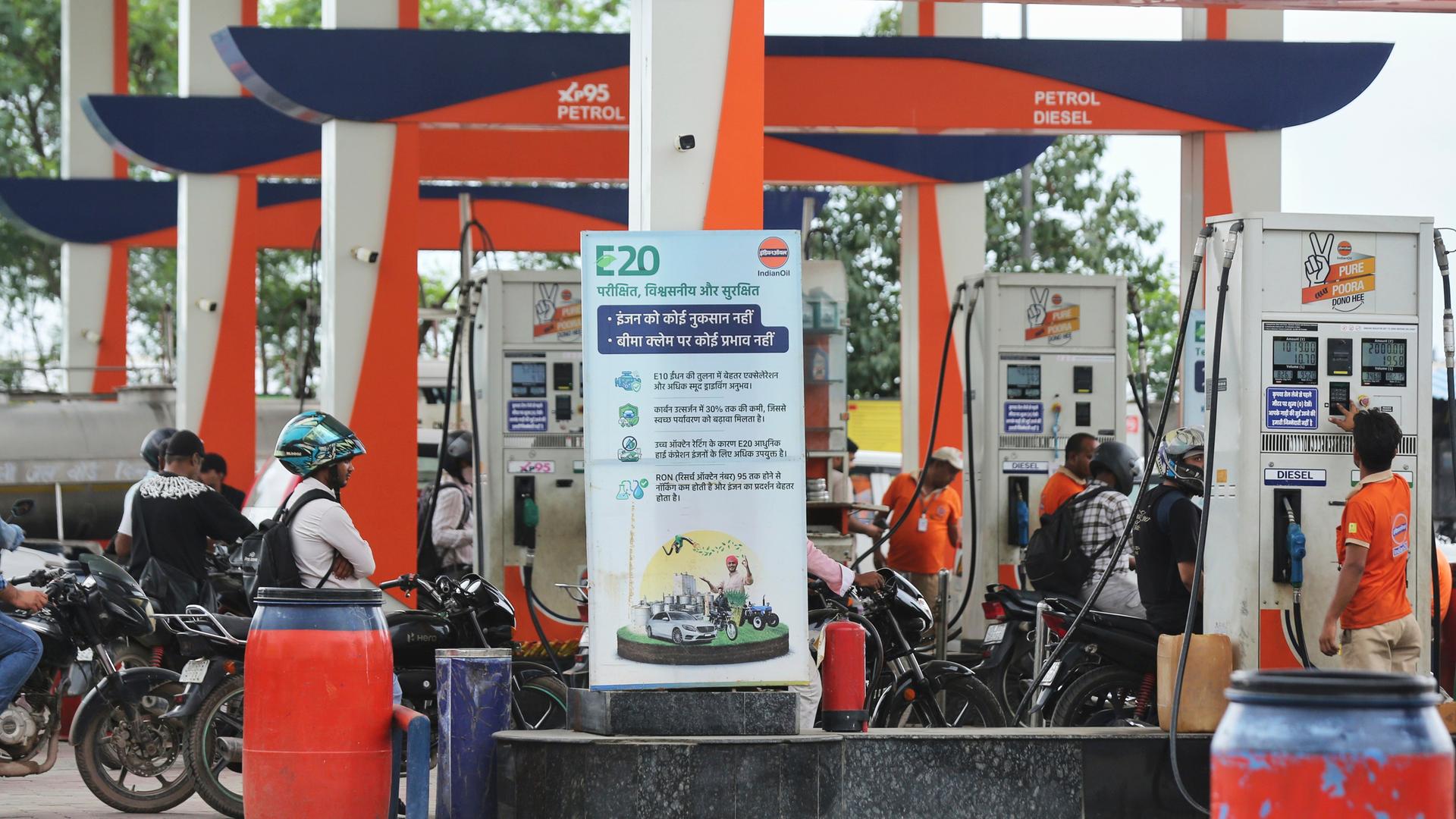 Neu-Delhi: Eine Werbetafel (M) wirbt für die E20-Kraftstoffpolitik, während sich Autofahrer an einer Tankstelle in der indischen Hauptstadt zum Tanken anstellen.