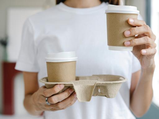 Mensch mit zwei Coffee-to-go-Bechern. 
