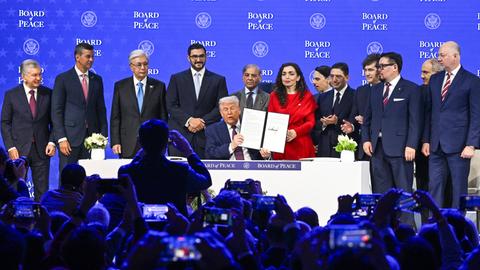 Eine Reihe an Premierministern und Prsäidenten stehen auf einer Bühne hinter Trump. Der US-Präsident hält einen unterschriebenen Vertrag in die Kameras