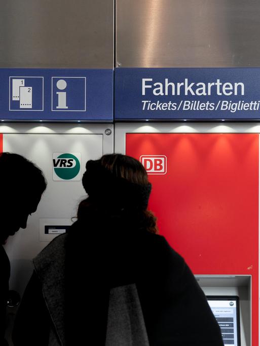 Zwei Personen stehen vor einem Fahrkartenautomat der Deutschen Bahn.