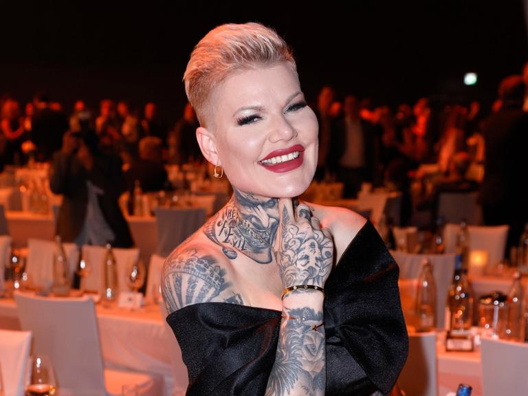 Melanie Müller in einem schwarzen Abendkleid. Sie schaut in die Kamera und lacht.