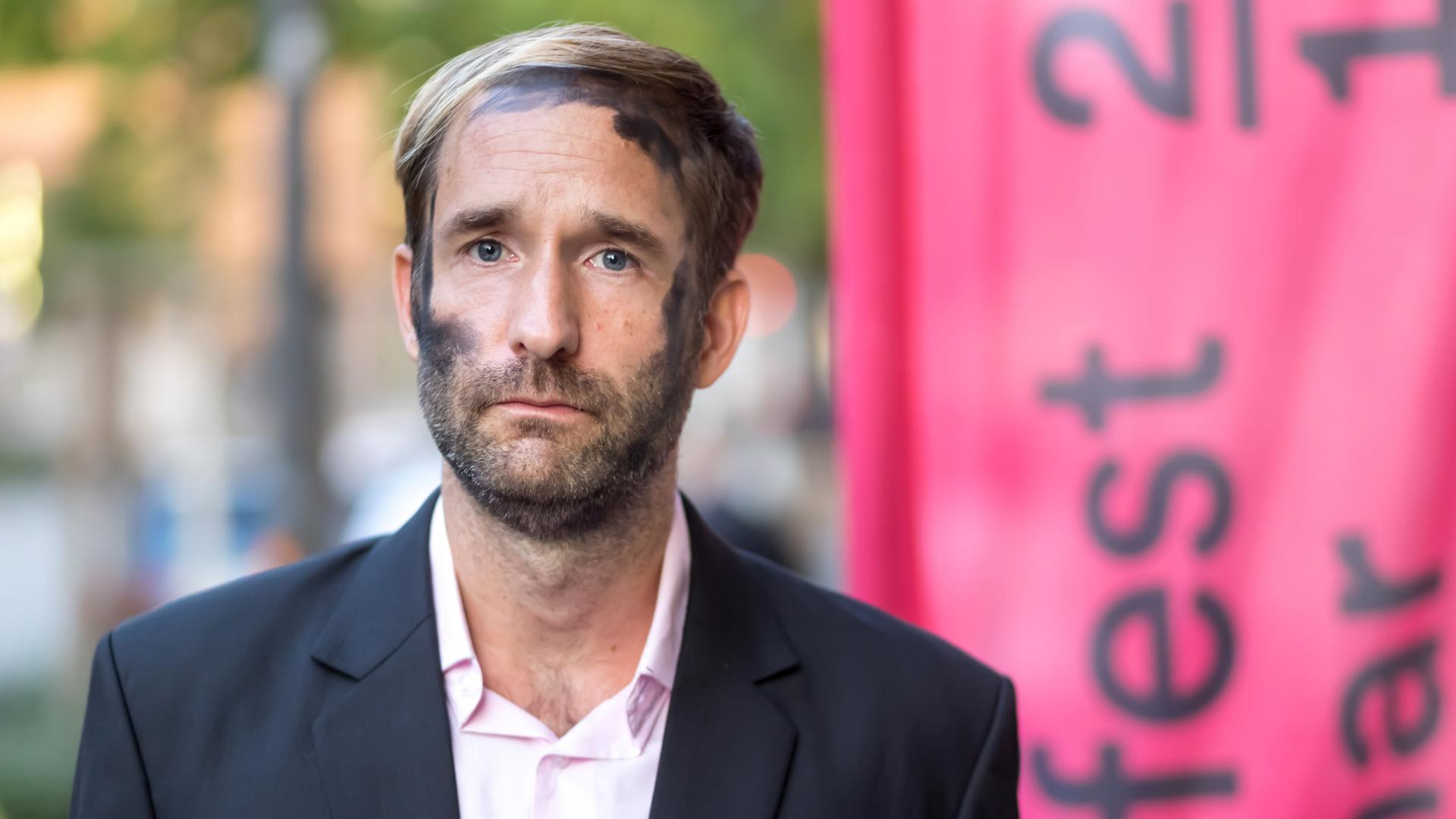 Philipp Ruch blickt ernst frontal in die Kamera. In seinem Gesicht sind die schwarzen Kohlespuren zu sehen, die er bei Aktionen des Zentrums für Politische Schönheit traditionell trägt Philipp Ruch blickt ernst frontal in die Kamera. In seinem Gesicht sind die schwarzen Kohlespuren zu sehen, die er bei Aktionen des Zentrums für Politische Schönheit traditionell trägt
