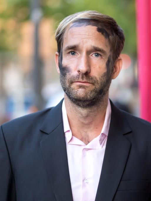 Philipp Ruch blickt ernst frontal in die Kamera. In seinem Gesicht sind die schwarzen Kohlespuren zu sehen, die er bei Aktionen des Zentrums für Politische Schönheit traditionell trägt