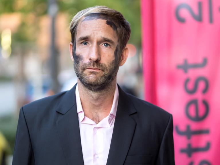 Philipp Ruch blickt ernst frontal in die Kamera. In seinem Gesicht sind die schwarzen Kohlespuren zu sehen, die er bei Aktionen des Zentrums für Politische Schönheit traditionell trägt