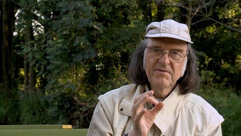 Ein Mann mit schulterlangen Haaren und Kappe erklärt etwas mit den Händen gestikulierend, während er im Kahn durch den Spreewald gleitet
