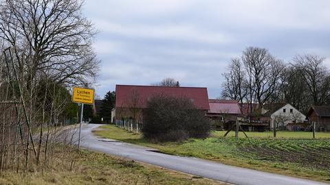 Das Ortseingangsschild des Lychener Ortsteiles Rutenberg: Zu sehen ist eine Landstraße, hinten einige Häuser.