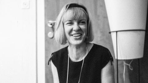 Schwarzweißaufnahme von Ingeborg Bachmann, die lachend in einem Salon sitzt