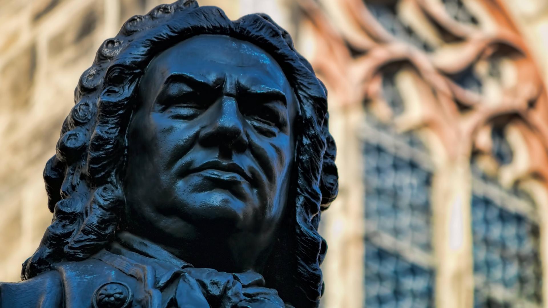 Blick auf das Gesicht des in Leipzig stehenden Denkmals von Johann Sebastian Bach. Hinter ihm kann man Fenster und Wände der Thomaskirche erkennen. 