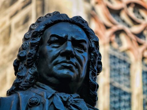 Blick auf das Gesicht des in Leipzig stehenden Denkmals von Johann Sebastian Bach. Hinter ihm kann man Fenster und Wände der Thomaskirche erkennen. 