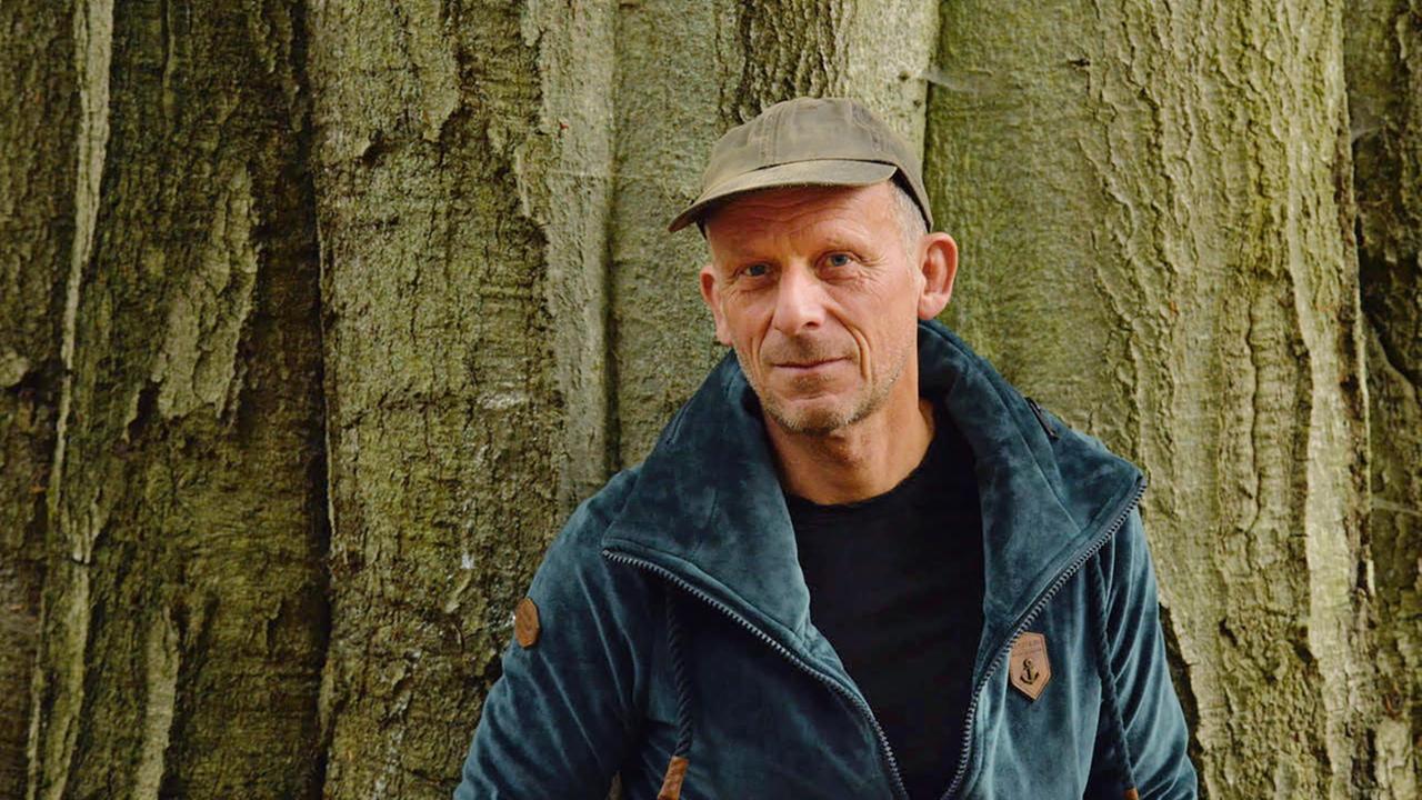 Martin Hansen, mit kurzen Haaren und einer Basecap, steht vor einem Baumstamm.