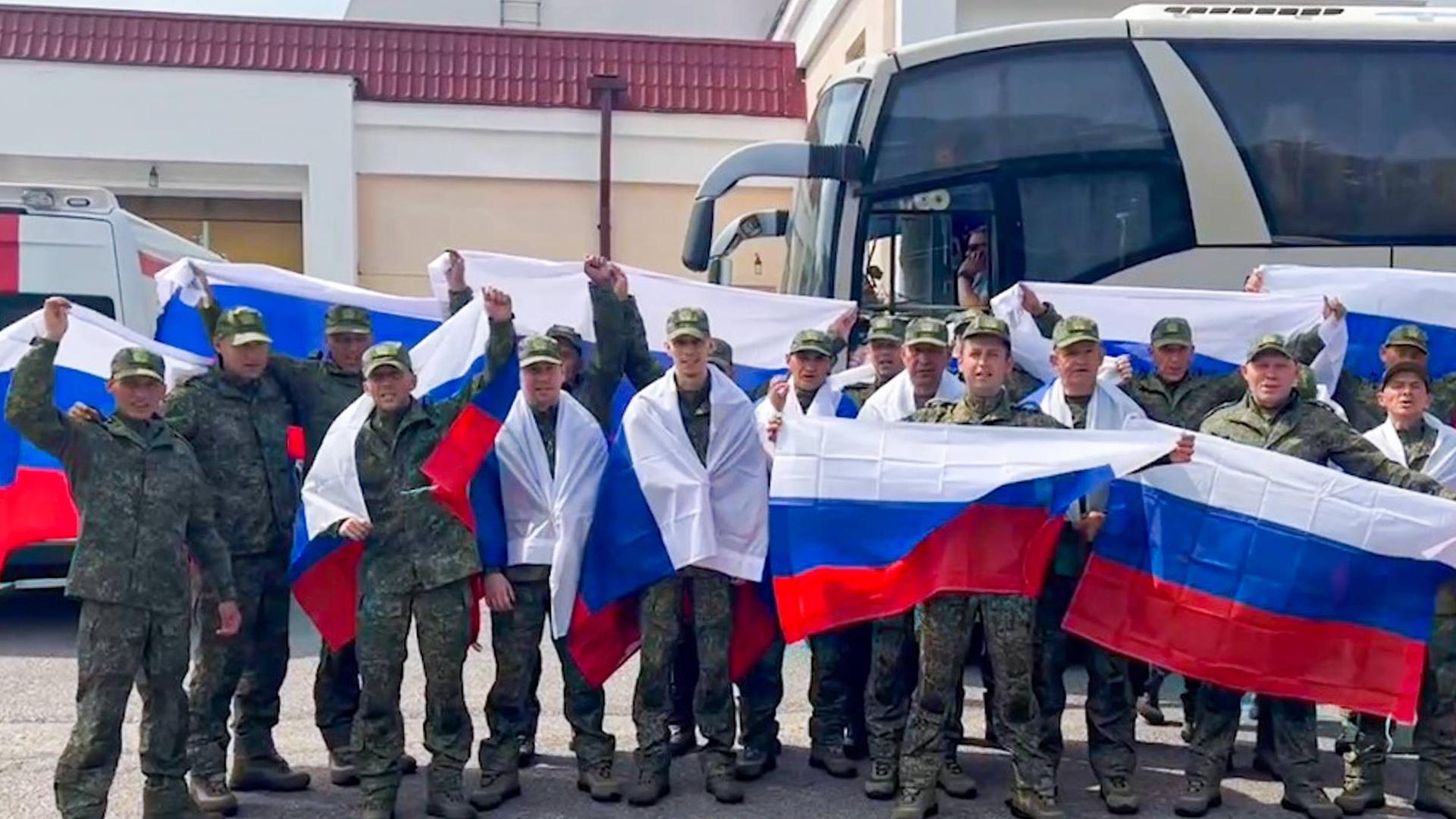 Soldaten mit russischen Fahnen stehen vor einem Bus. 