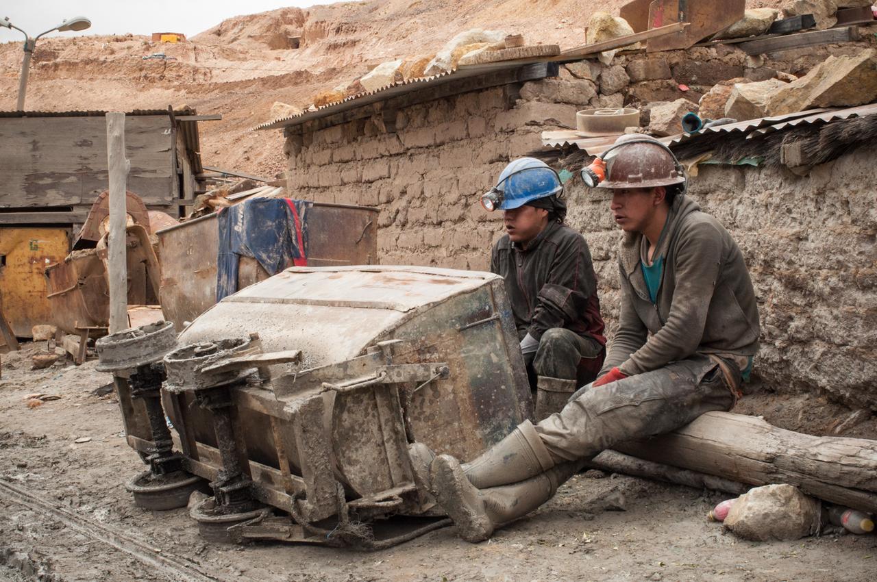 Zwei Minenarbeiter mit Helm sitzen vor einem umgekippten Transportwagen
