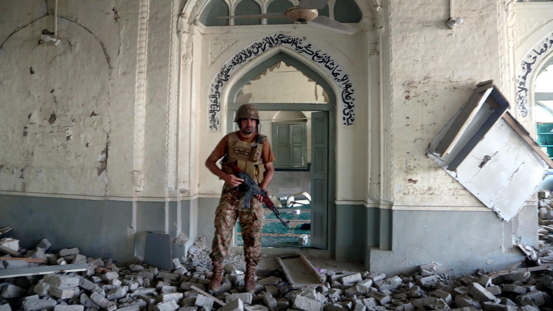 Ein Soldat steht am Eingang einer Moschee. Überall sind Trümmer.