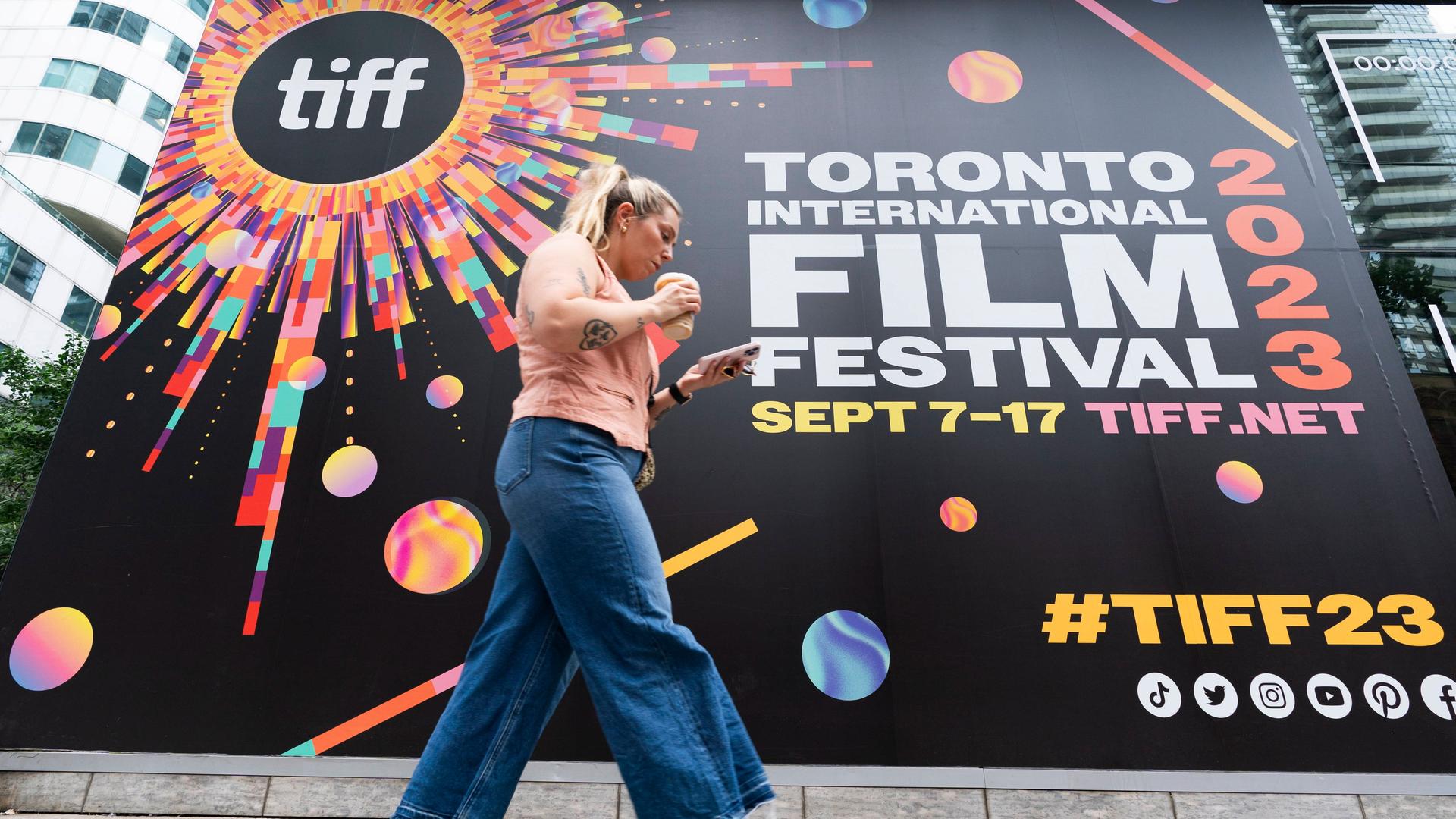 Das Bild zeigt eine Frau, die an einem Plakakt zum "Toronto International Film Festival 2023" vorbeiläuft.
