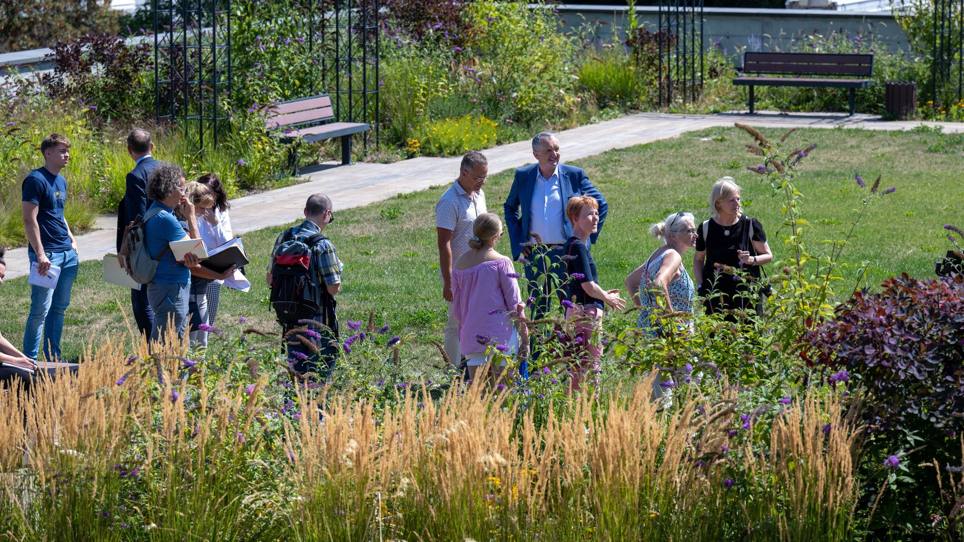 Mehrere Menschen stehen in einem grünen Stadtgarten.