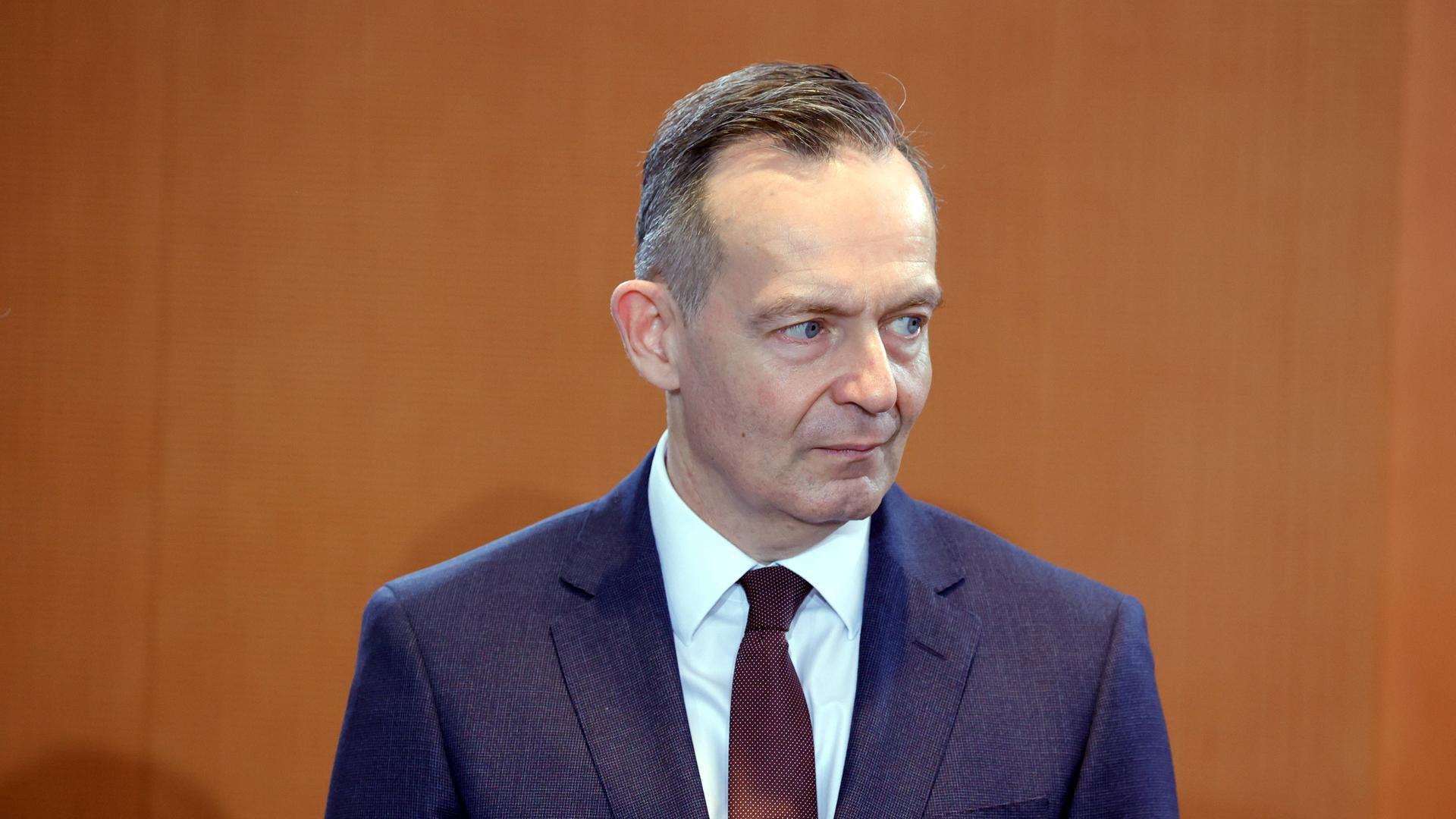 Dr. Volker Wissing, Bundesminister für Digitales und Verkehr, fotografiert vor holzfarbener Wand. Er blickt zum rechten Bildrand.