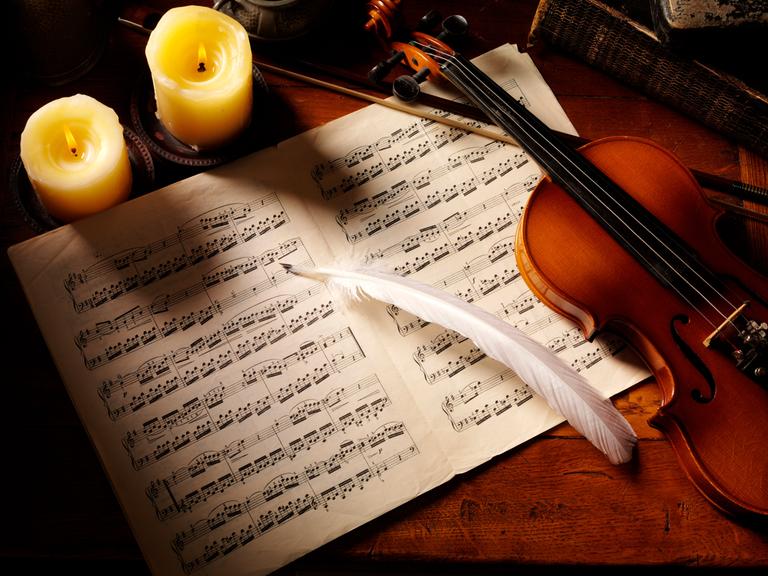 Violine auf Notenblättern mit Feder, von Kerzen illuminiert Violine auf Notenblättern mit Feder, von Kerzen illuminiert