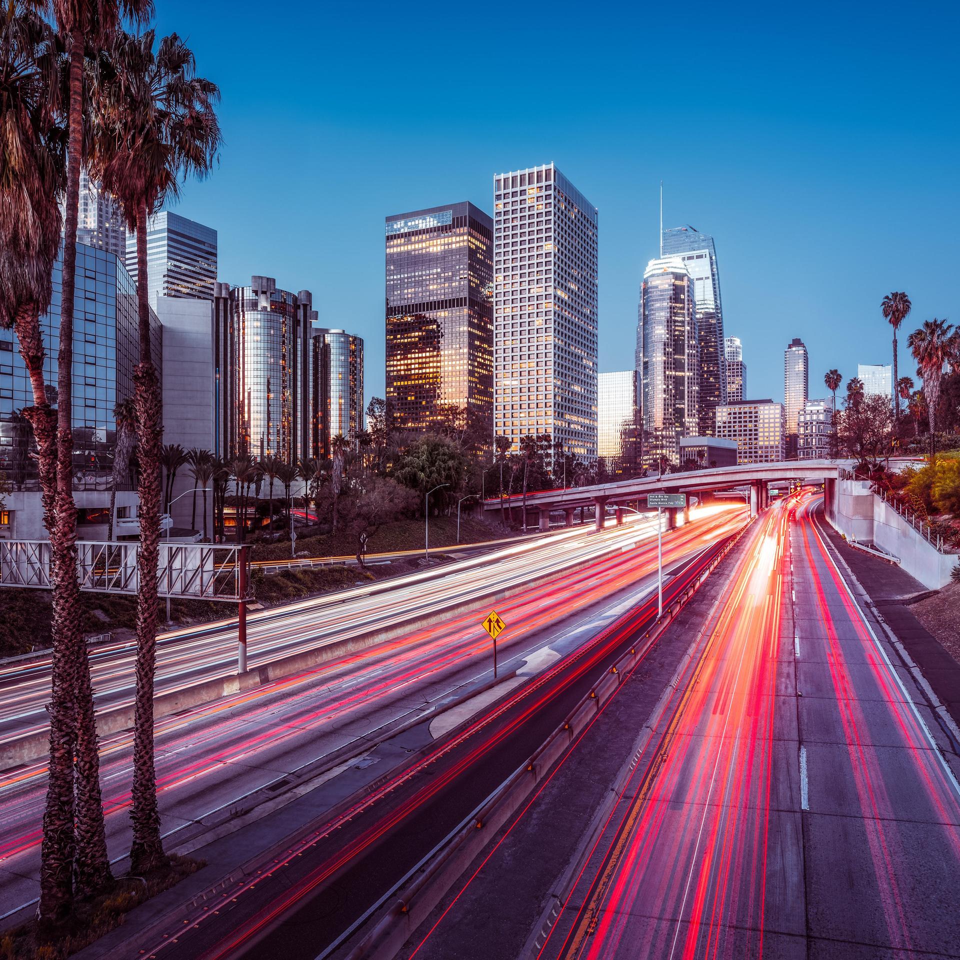 Die Skyline von Los Angeles bei Nacht mit bunt leuchtendem Highway und Wolkenkratzern.