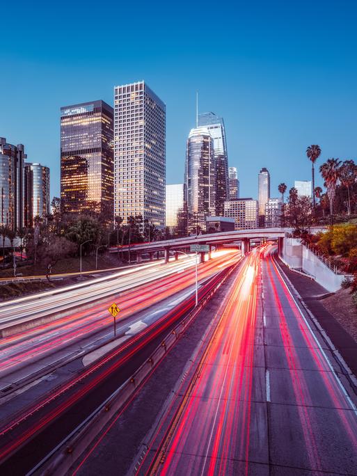 Die Skyline von Los Angeles bei Nacht mit bunt leuchtendem Highway und Wolkenkratzern.